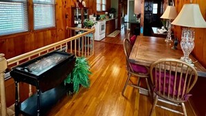 A spacious room with wooden walls and floors, a dining table with chairs, a ceiling fan, and a piano. - Cozy Mtn. Home in Newland (Newland)