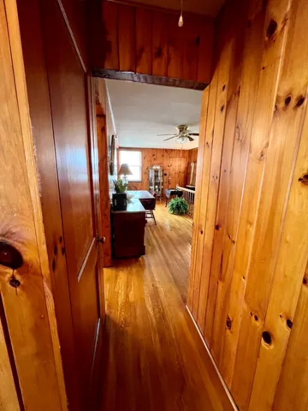 Un pasillo interior de madera con un ventilador de techo, un comedor con mesa y sillas, y una cocina con estufa y armarios.