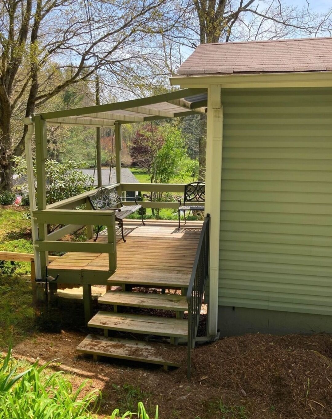 Een overdekt buitengebied met een houten terras, een bank en een kleine tafel.