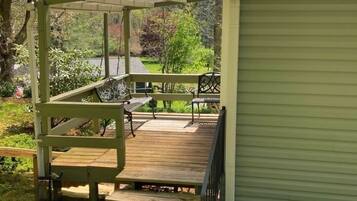 Een overdekt buitengebied met een houten terras, een bank en een kleine tafel.