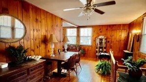 A wooden-paneled room with a dining table, chairs, a ceiling fan, and a mirror. - Cozy Mtn. Home in Newland (Newland)