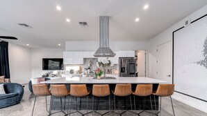 A modern kitchen with a central island, bar stools, and a large window. - Modern Austin home w private pool and spa, Minutes to Lake Austin & Lake Travis! (Austin)