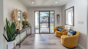 A modern living room with a sofa, a chair, a console table with plants, a large mirror, and a door leading to an outdoor area. - Modern Austin home w private pool and spa, Minutes to Lake Austin & Lake Travis! (Austin)