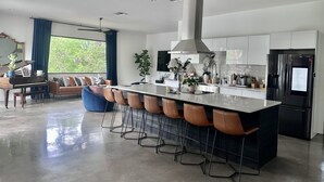 A modern kitchen with a central island, bar stools, and a large window. - Modern Austin home w private pool and spa, Minutes to Lake Austin & Lake Travis! (Austin)