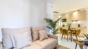 Ein modernes Wohnzimmer mit einem beigen Sofa, einem Couchtisch und einem Essbereich mit gelben Stühlen.