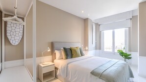 Ein modernes Schlafzimmer mit einem großen Bett, Nachttischlampen, einer Pendelleuchte und Blick ins Freie durch ein Fenster.