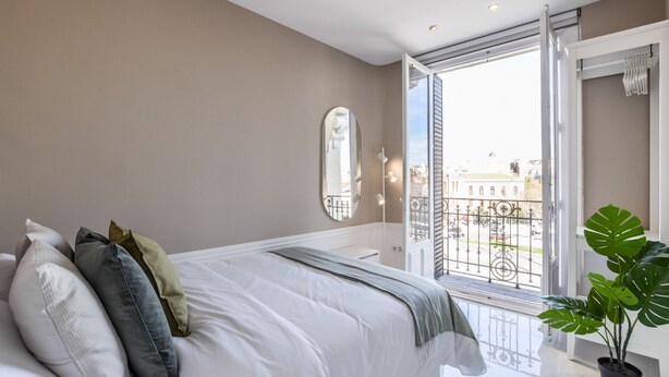Ein Schlafzimmer mit einem großen Bett, einem Blumentopf, einem Balkon mit Blick auf Gebäude und einer Schiebetür.
