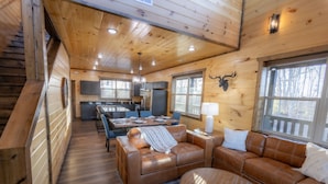 A cozy cabin interior with a dining area, a sofa, and a fireplace.