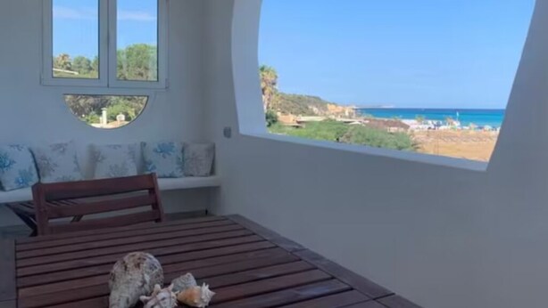 A room with a wooden table, a bench, and a large window offering a view of the sea and landscape. - Simius beach - [Free Parking] (Simius)