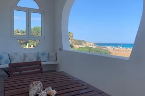 Une pièce avec une table en bois, un banc et une grande fenêtre donnant sur la mer et le paysage.