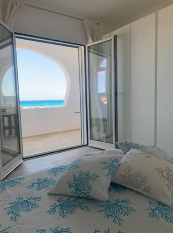 Une chambre avec un lit, une vue sur la plage et une porte-fenêtre coulissante donnant sur un espace extérieur.