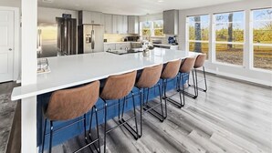 Une cuisine moderne dotée d’un grand îlot central, de tabourets de bar et offrant une vue sur un vignoble grâce à de grandes fenêtres.