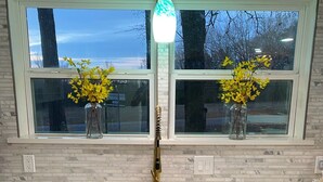 Une cuisine dotée d’un plan de travail en marbre blanc, d’un robinet doré et de deux fenêtres ornées de fleurs jaunes.
