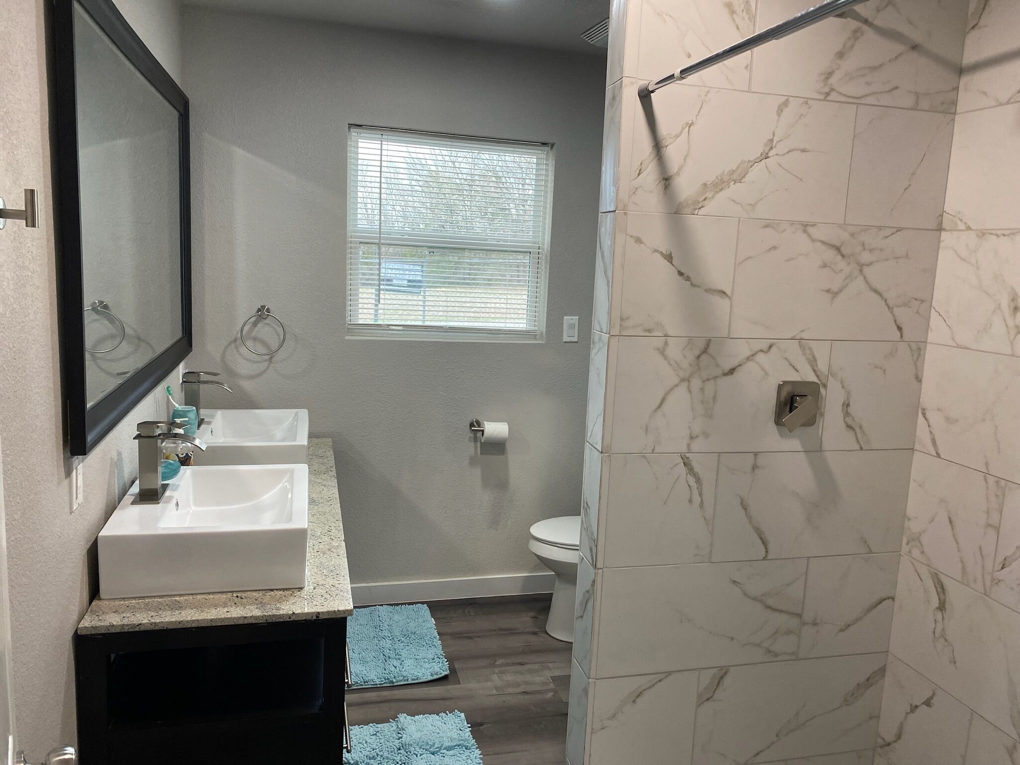 A bathroom with two sinks, a toilet, a window, and a shower area.