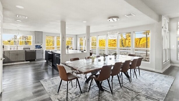 Un vaste espace dédié à la salle à manger, avec une grande table et des chaises, une cuisine en arrière-plan et de grandes fenêtres offrant une vue sur les arbres aux couleurs automnales.