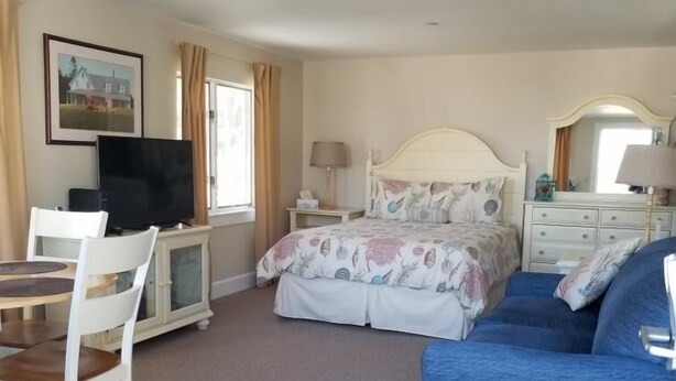 A bedroom with a bed, a blue sofa, a desk with a TV, and a dresser. - Sheepscot Harbour Studio #215 (Edgecomb)