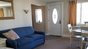 A room with a bed, a blue sofa, a dining table with chairs, a door, and a window with curtains. - Sheepscot Harbour Studio #215 (Edgecomb)