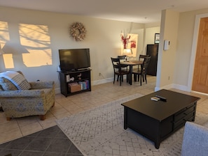 A living room with a sofa, a coffee table, a TV, and a dining area with chairs and a table.