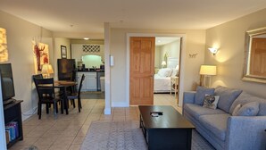 A living room with a sofa, coffee table, and TV stand. There is a dining area with chairs and a table. The kitchen is visible in the background with cabinets and appliances. - Sheepscot Harbour Studio #205 (Edgecomb)