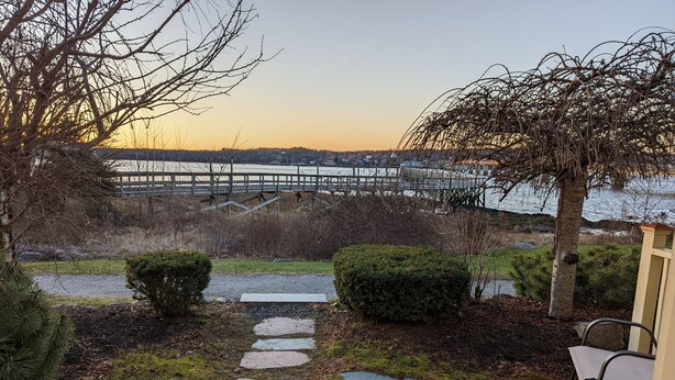A garden pathway leading to a wooden deck with a view of a bridge over water. - Sheepscot Harbour Studio #205 (Edgecomb)