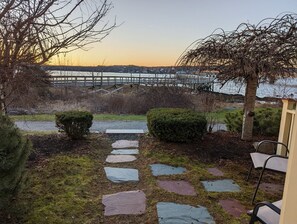 A stone pathway leading to a wooden deck overlooking a river, with a bridge in the background.