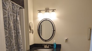 A bathroom with a vanity, a round mirror, a sink, and a shower curtain. - Sheepscot Harbour Studio #205 (Edgecomb)