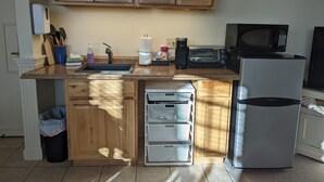 A kitchen with wooden cabinets, a sink, a toaster, a microwave, and a refrigerator. - Sheepscot Harbour Studio #308 (Edgecomb)