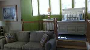 A cozy living room with a striped sofa, a small table with a lamp, and a staircase leading to a bedroom with a bed. - Sheepscot Harbour Studio #308 (Edgecomb)