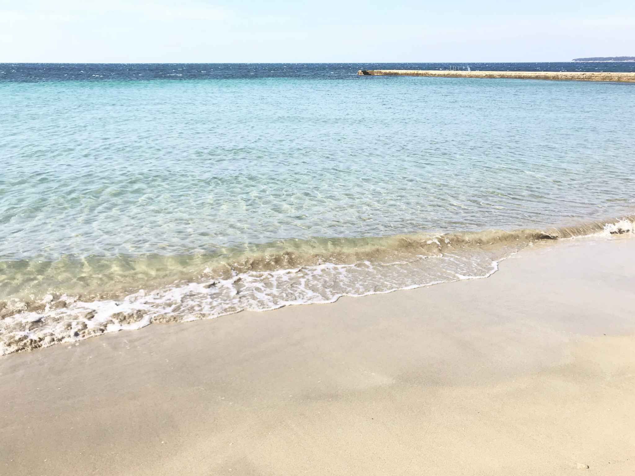 A beach with clear shallow waters and a sandy shore.