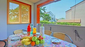 Un balcón con una mesa dispuesta para dos personas, con mantel de flores, sillas de mimbre y una bandeja de frutas.
