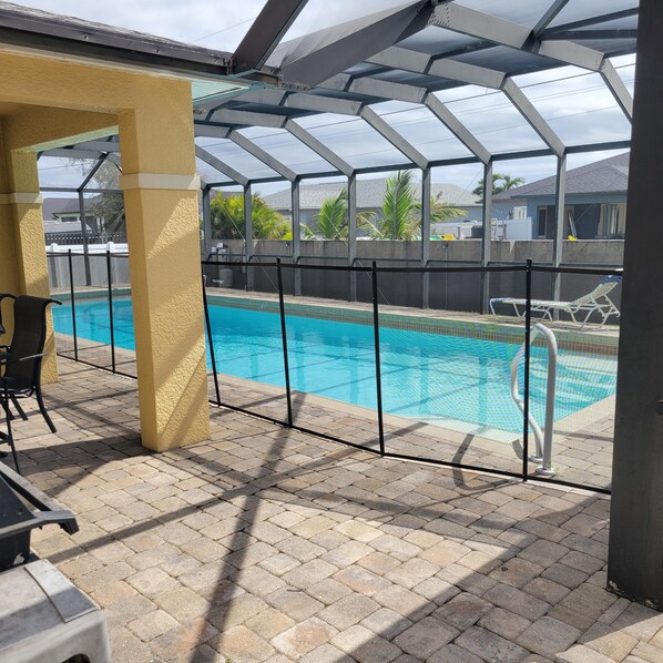 Une piscine extérieure couverte, dotée d’un toit en verre, entourée d’une terrasse en briques et agrémentée de quelques chaises longues.