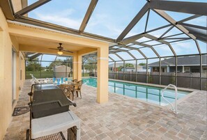 Un espace piscine extérieur doté d’un patio couvert, d’un barbecue et de coins salon.