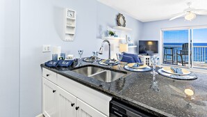 Een keuken met een dubbele spoelbak, witte kastjes en uitzicht op de oceaan door een groot raam.