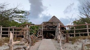A thatched-roof structure with a wooden gate leading to a sandy path. - Tambo Marina Ecohostal - Hostel (Santa Catalina)