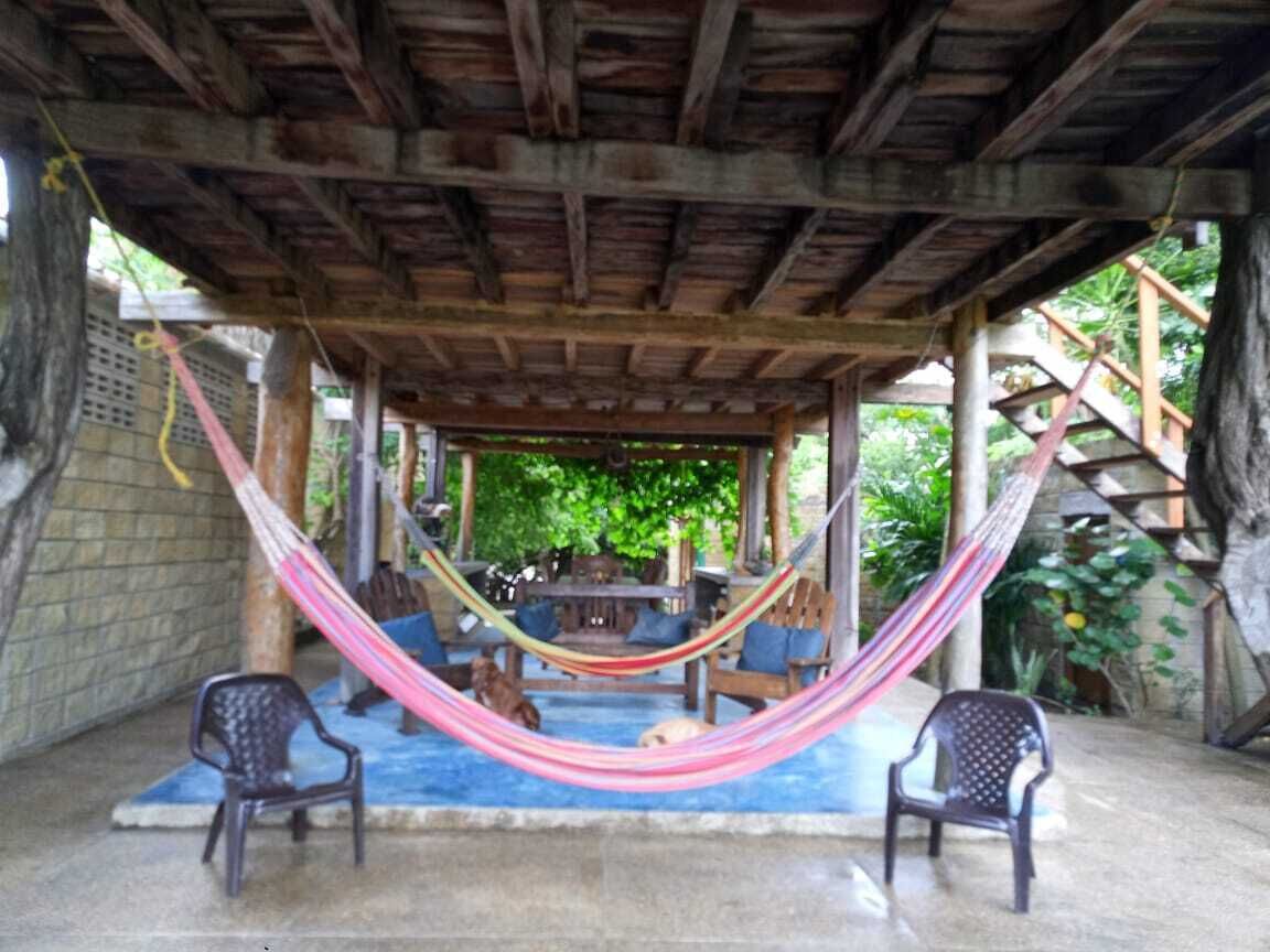 Un espacio de estar al aire libre con techo, una hamaca, dos sillas y una piscina.