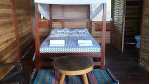 A wooden cabin with a single bed, a small table, and a mosquito net. - Tambo Marina Ecohostal - Hostel (Santa Catalina)