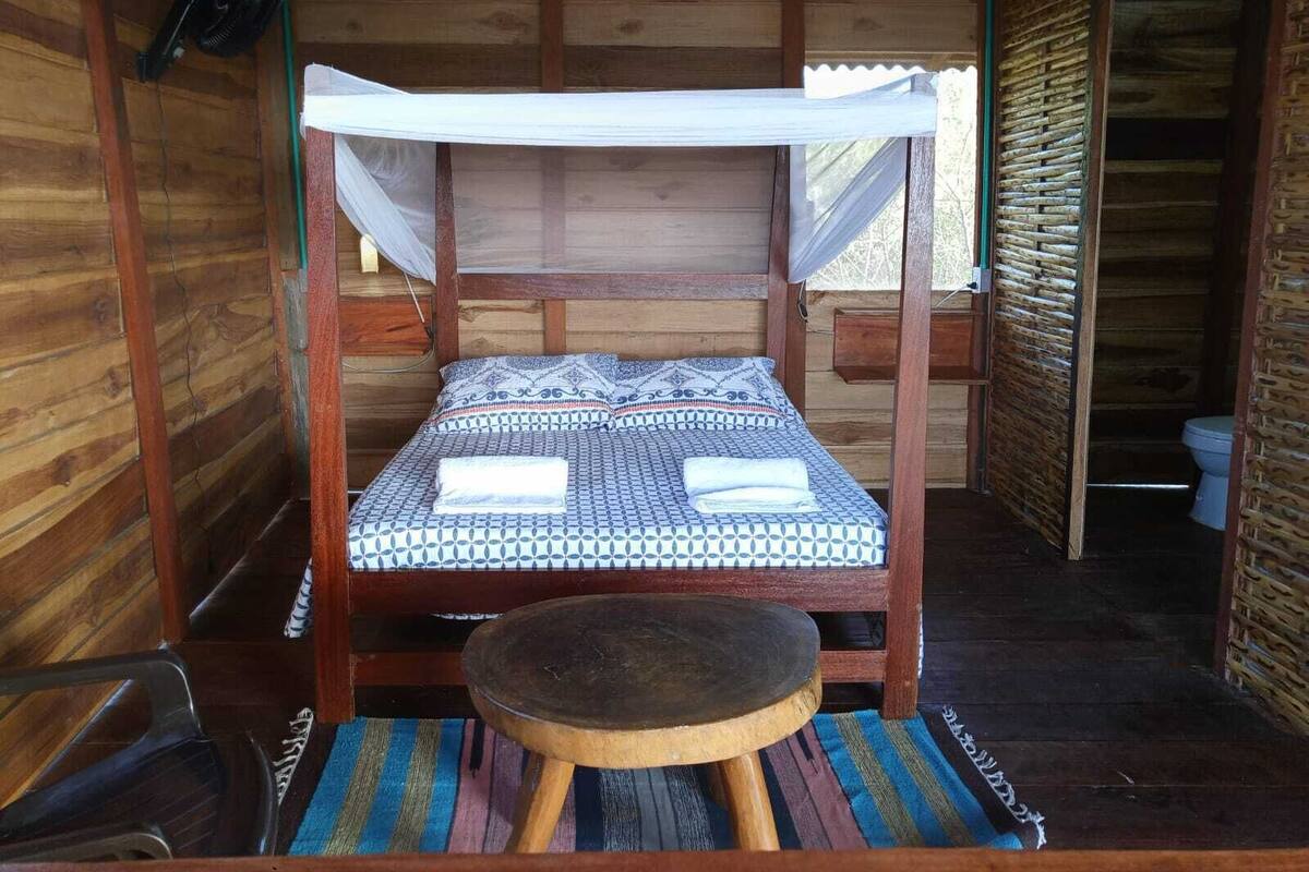 Una cabaña de madera con una cama individual, una mesita y un mosquitero.
