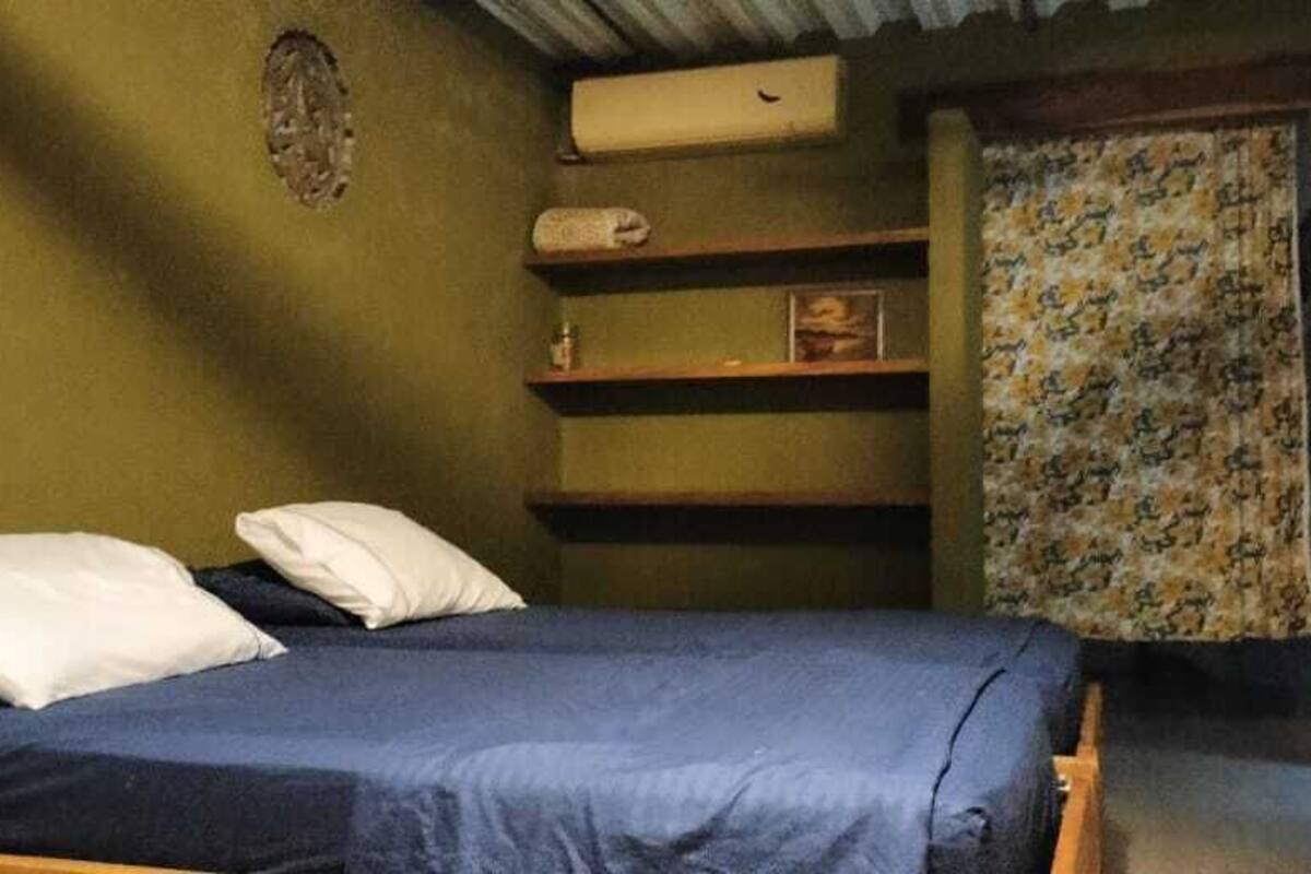 Una cama individual con colchón azul y almohadas blancas en una habitación con paredes verdes.