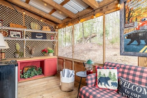 A cozy cabin interior with a wooden ceiling, a red bench, a table with a lantern, and a large window offering a forest view. - Pond View! Great Location! Close to Attractions Family and Pet Friendly! (Sevierville)