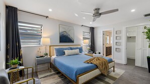 Ein modernes Schlafzimmer mit Bett, Nachttischen, Deckenventilator und Blick ins Bad.