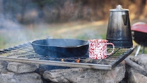 A metal table with a black pan, a red and white speckled mug, and a black pot on a metal grate. - Two cozy pods with water tower (Kingston)
