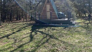 A small wooden cabin with a sloped roof, surrounded by trees and a grassy area. - Two cozy pods with water tower (Kingston)
