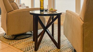 Een kamer met twee beige fauteuils, een klein rond tafeltje met een fles en een glas, en uitzicht op de zee door grote ramen.