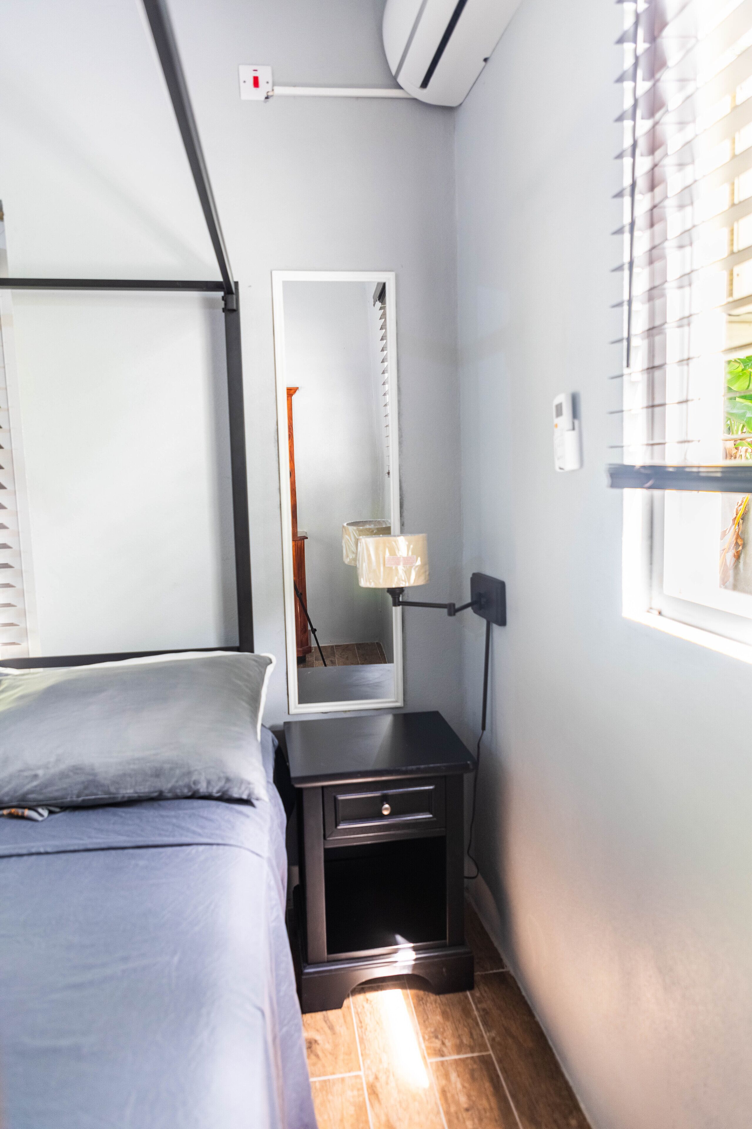 Une chambre à coucher avec un lit, une table de chevet, un miroir et une fenêtre avec des stores.