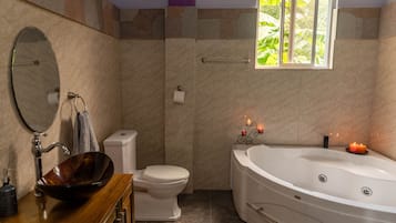 A bathroom with a wooden vanity, a round mirror, a toilet, and a freestanding bathtub with a candle.