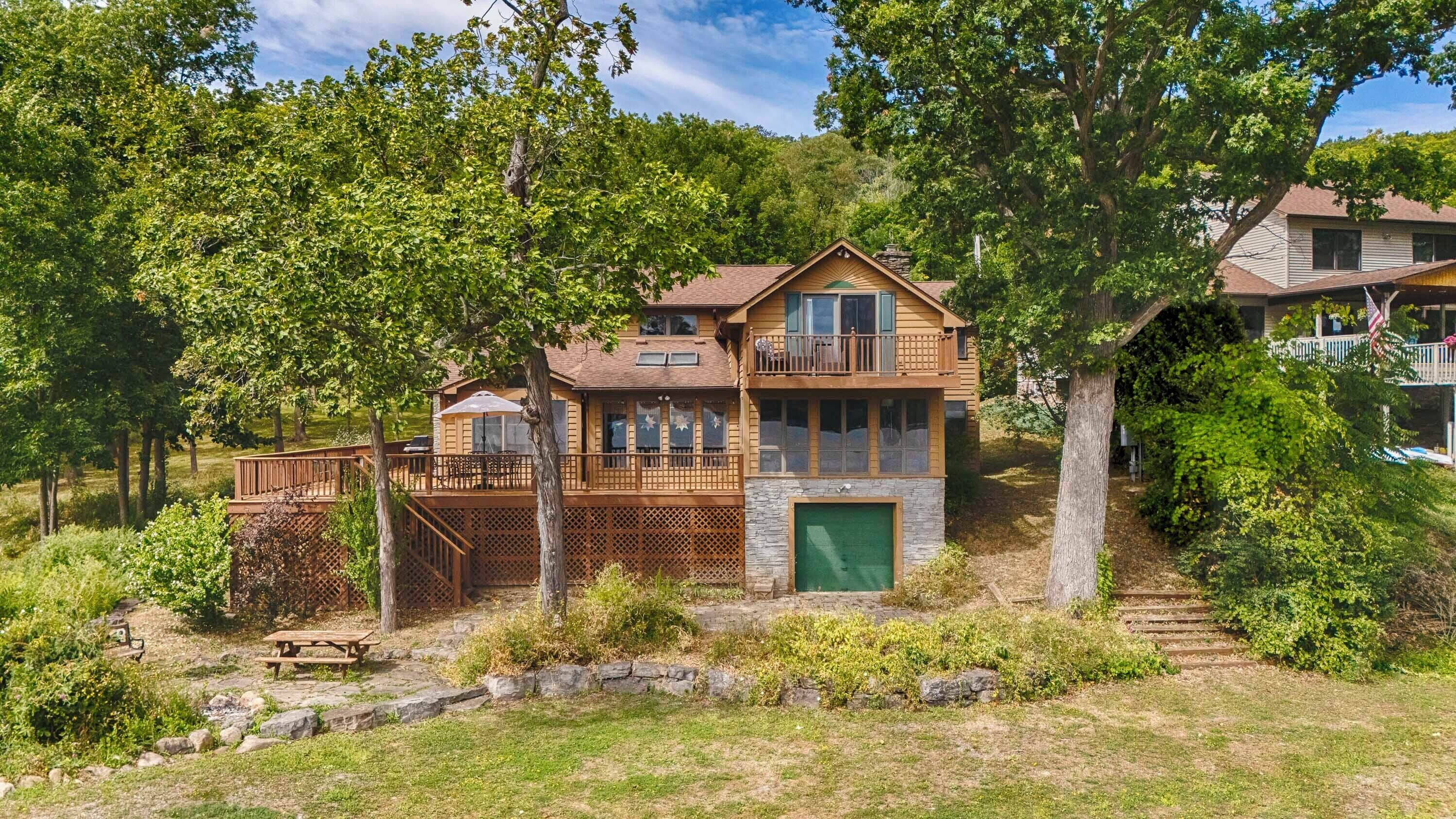 A two-story wooden cabin with a balcony, surrounded by trees and a stone pathway.