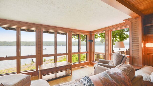 A spacious room with large windows offering a view of a lake and distant hills. There is a wooden bench, a cushioned sofa, and a lamp on a side table.