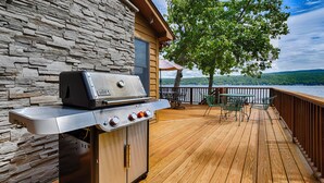 A wooden deck with a stone wall, a grill, and a view of a lake.