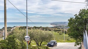 A road with a car parked on the side, a road sign, and a view of a coastal area with buildings and greenery. - S294 - Sirolo, wonderful three-room apartment with terrace and sea view (Sirolo)