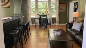 A cozy room with a bar area, a dining table with chairs, a leather sofa, and a coffee table. - Spacious PA Wilds Getaway! Water views, firepit w/ covered patio (Driftwood)